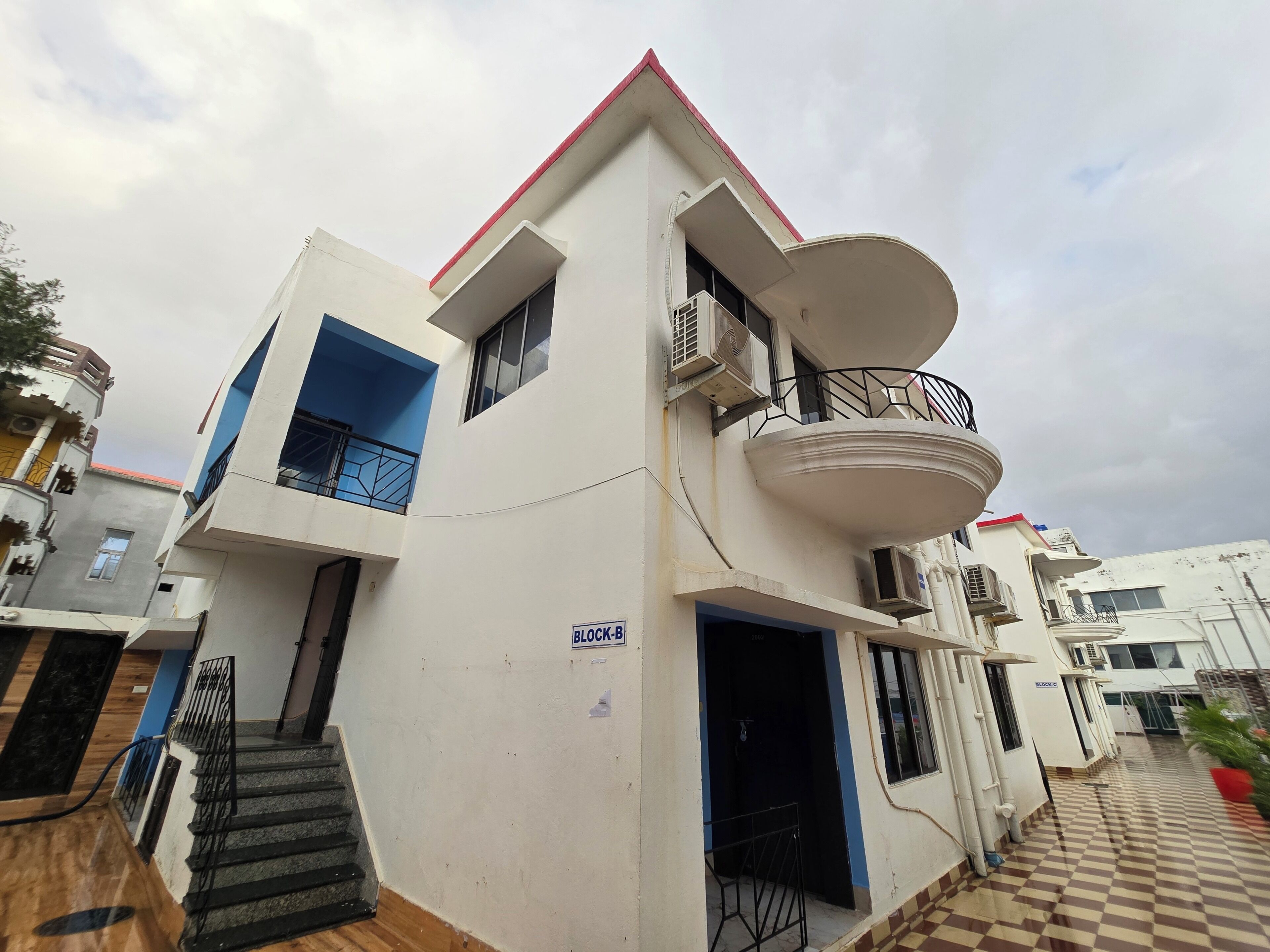 A multi-story residential building with a balcony, a staircase, and a checkered floor pattern.