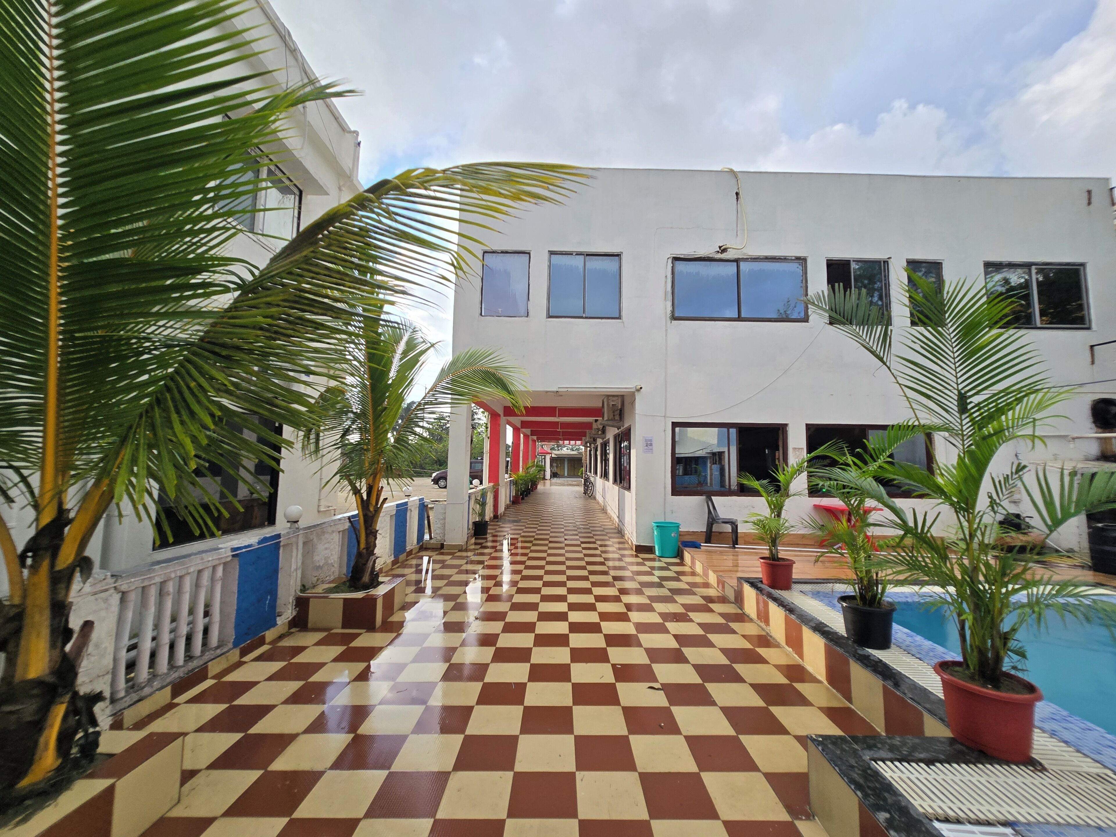 A hotel corridor with a checkered floor, potted plants, and a pool area.