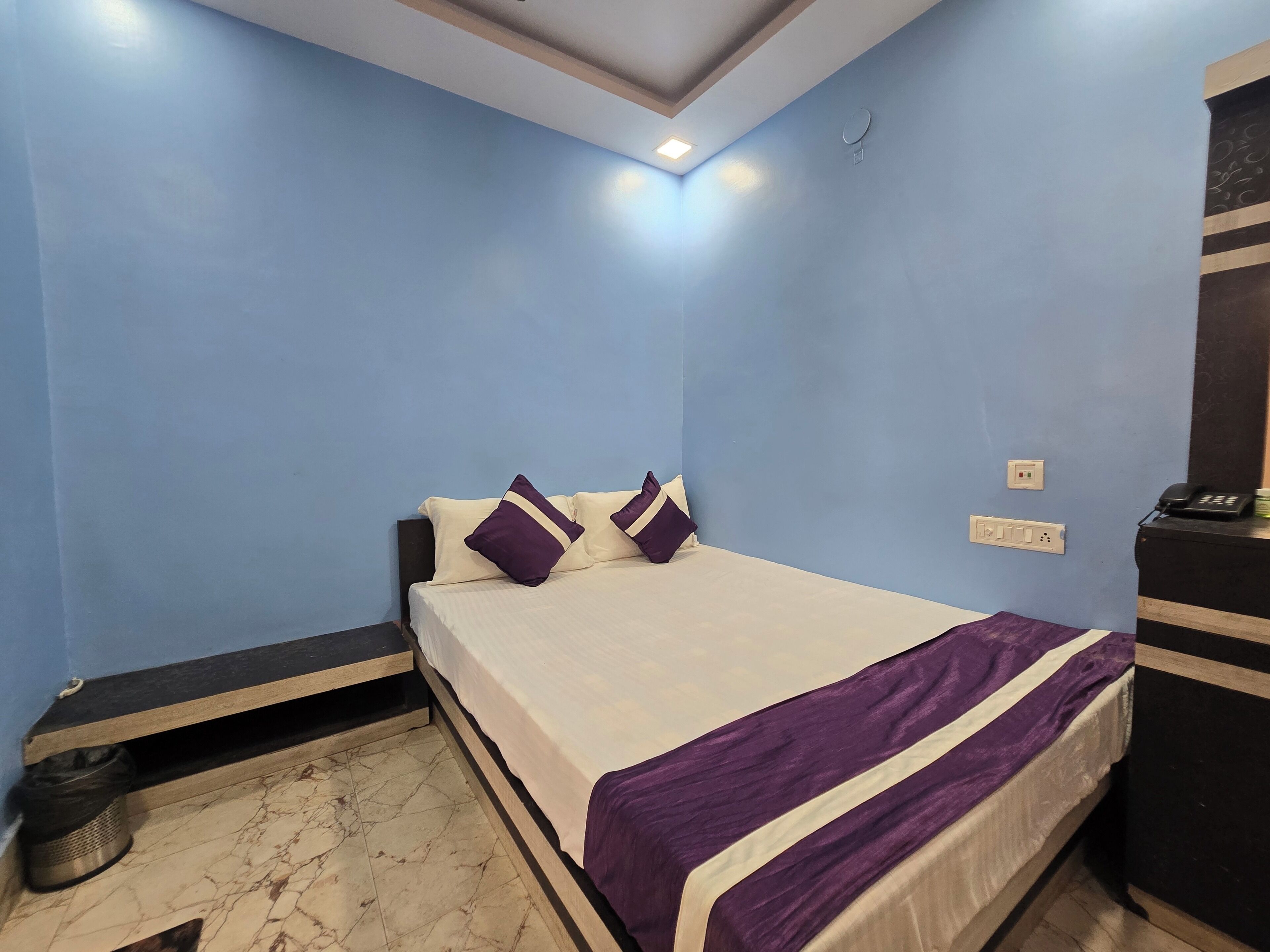 Un dormitorio con cama, un cubo de basura, un escritorio con teléfono y un enchufe de pared.