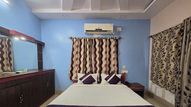 Una habitación de hotel con una cama, un armario, un equipo de aire acondicionado y cortinas estampadas.