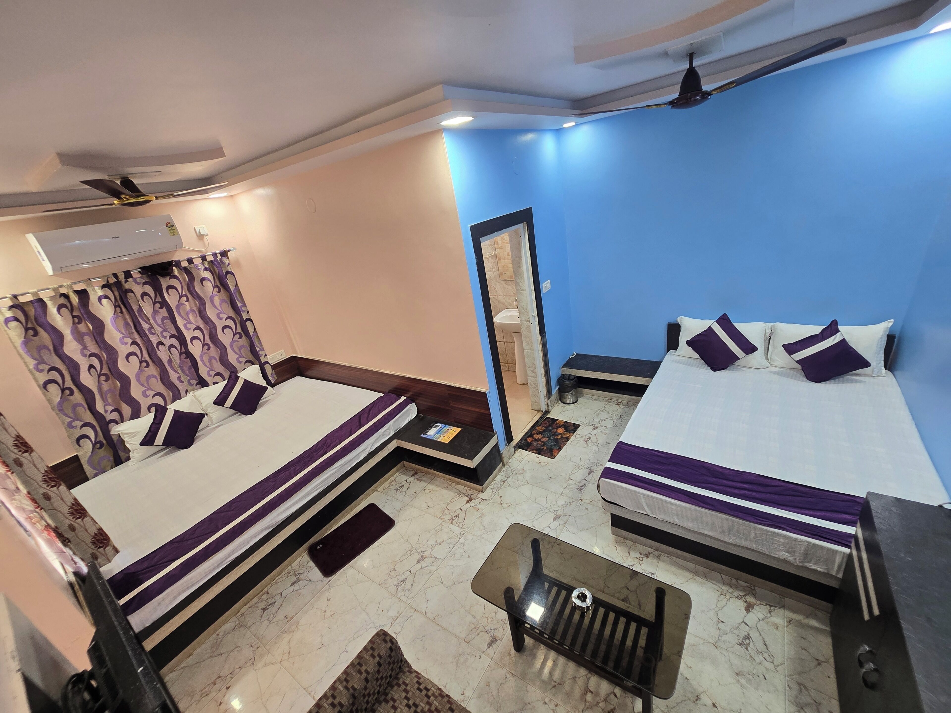 A hotel room with two beds, a small table, a mirror, and a ceiling fan.