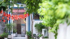 A storefront with a neon sign, red flags, and potted plants. - Ngoc Cherry (Hoa Lu)