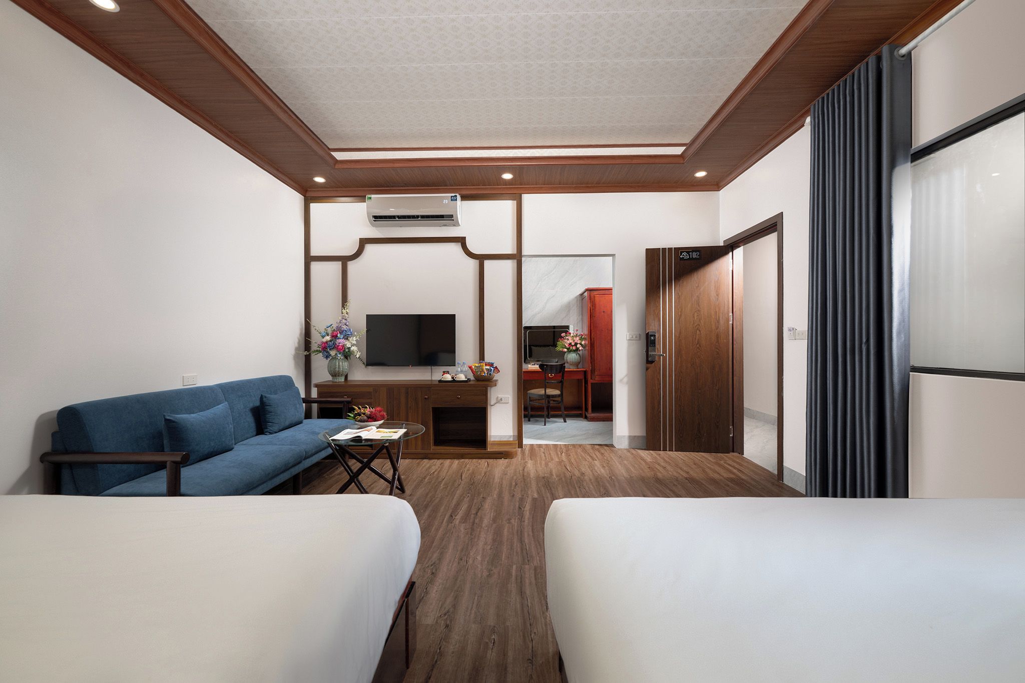 Habitación de hotel con sofá, una mesita con un florero, televisor y un armario de madera.
