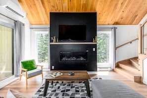 Ein modernes Wohnzimmer mit Kamin, Flachbildfernseher und Wendeltreppe.
