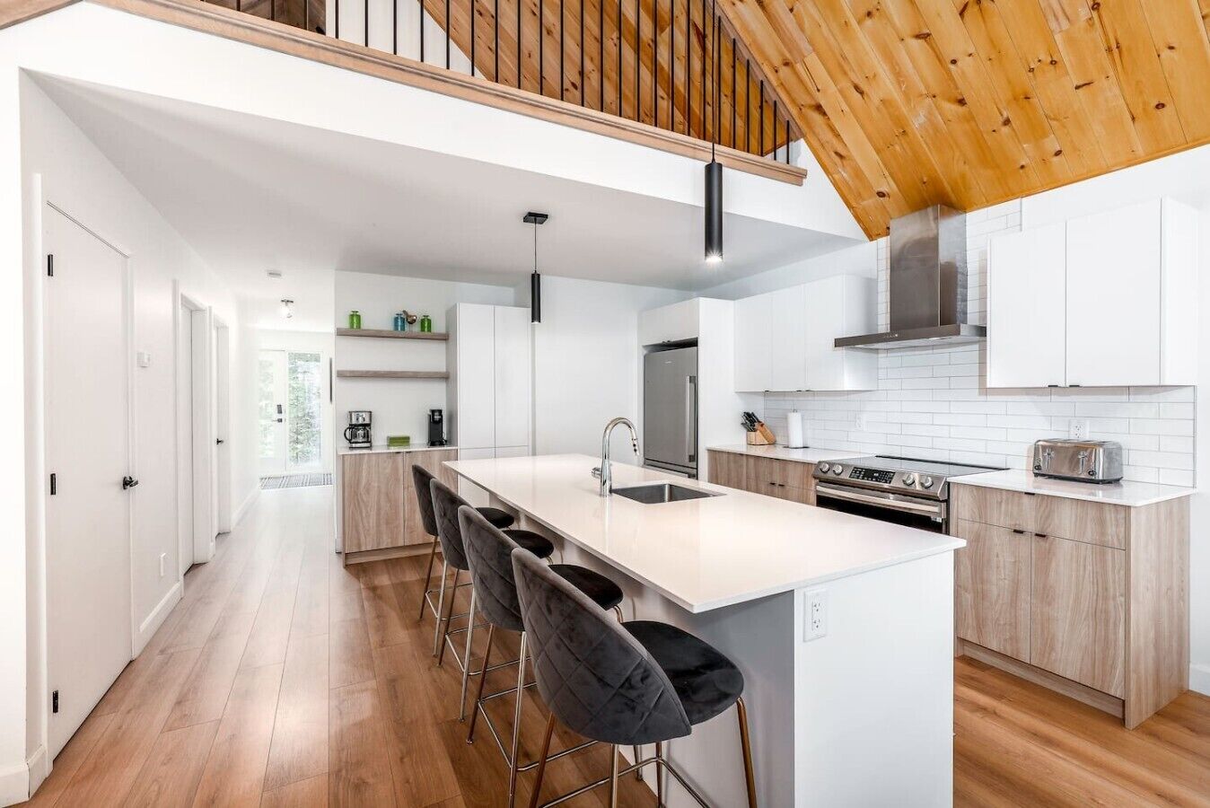 A modern kitchen with a central island, bar stools, and a wooden ceiling.