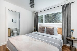 Quarto com cama, janela com cortinas, mesa de cabeceira e criado-mudo.