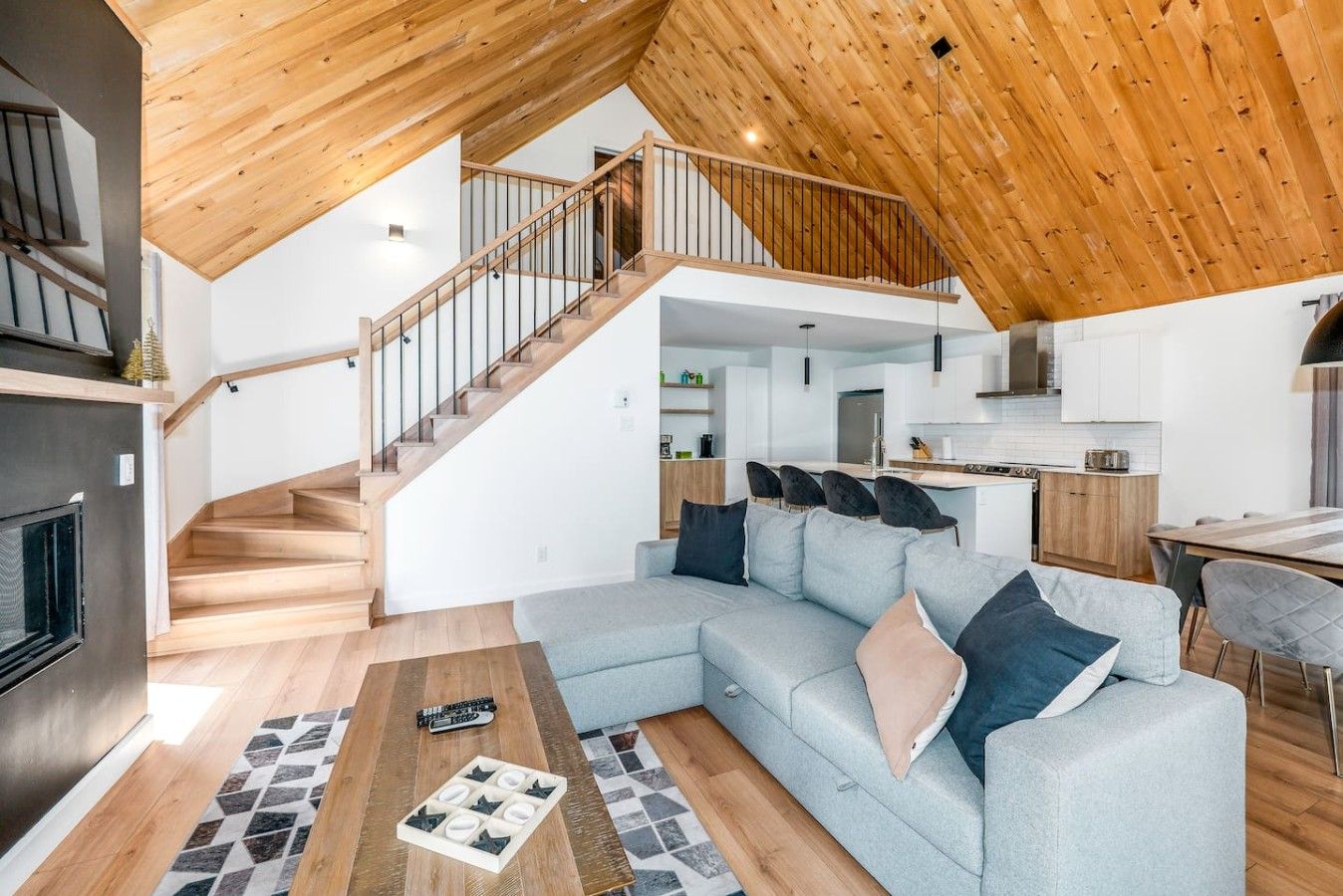 Un intérieur moderne avec un escalier en bois, un espace de vie comprenant un canapé et une table basse, et une cuisine en arrière-plan.