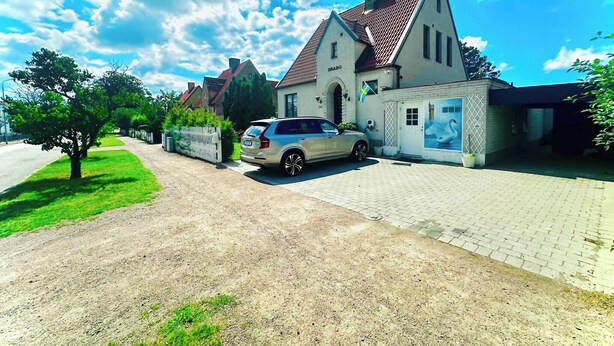 Ett hus med en asfalterad uppfart, en parkerad bil och en flagga.