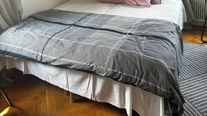 Ett sovrum med en säng, en platt-TV som är monterad på väggen, ett element och ett fönster med gardiner.