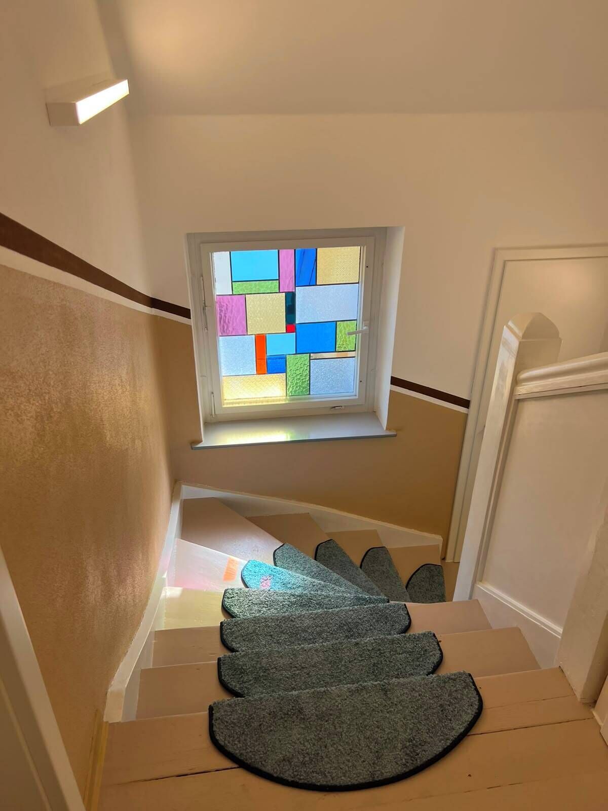 Eine Treppe mit Teppich und einem Fenster mit farbigen Glasfeldern.