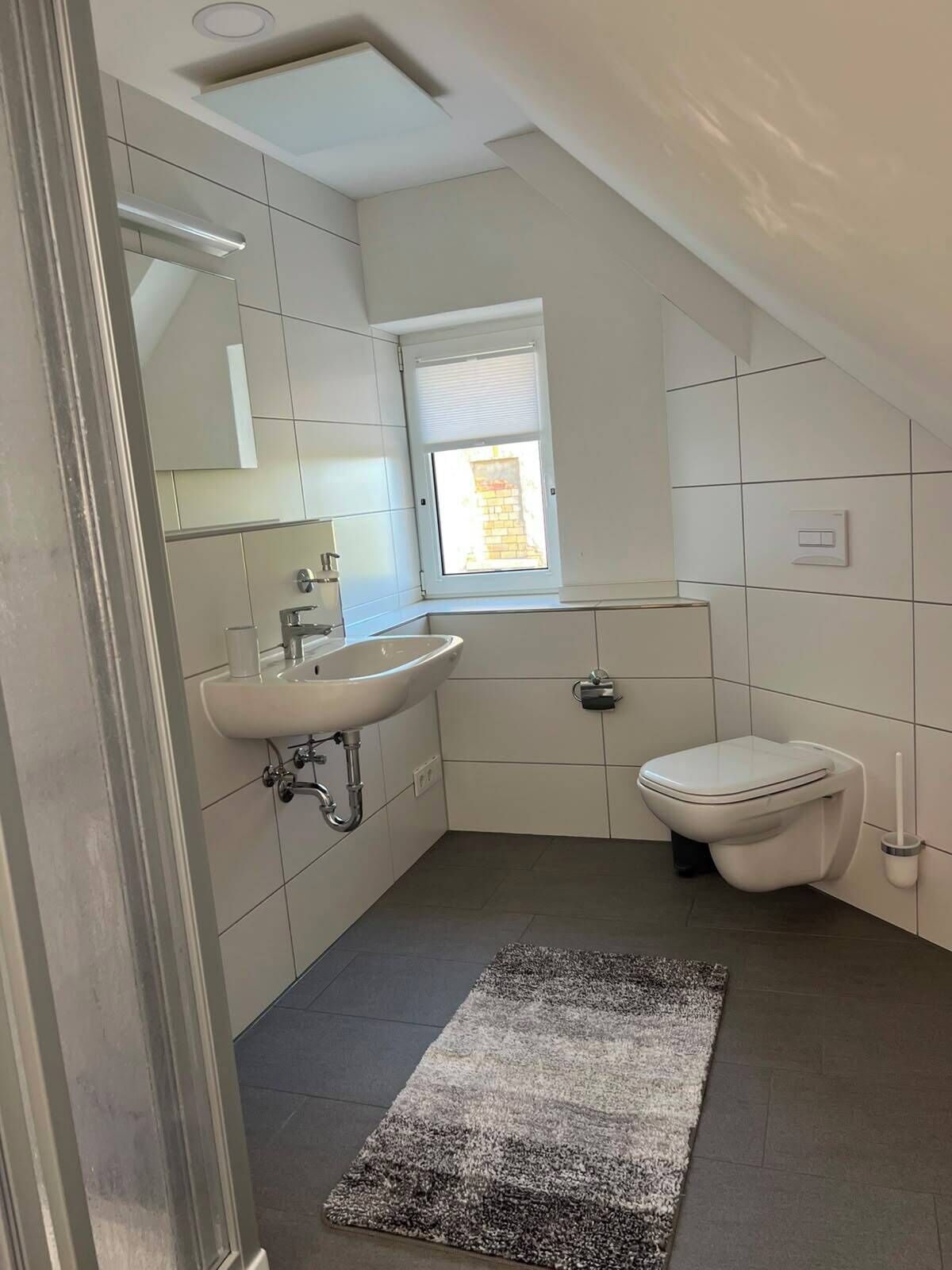 Un baño moderno con lavamanos, inodoro y un ventanal pequeño.