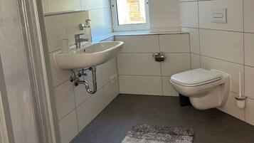 Un baño moderno con lavamanos, inodoro y un ventanal pequeño.