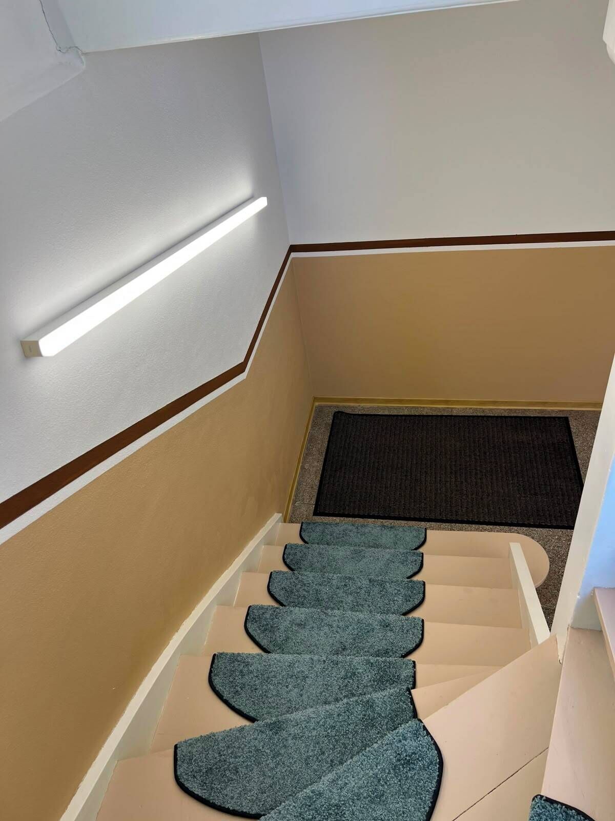 A staircase with a carpeted landing and a light fixture above.