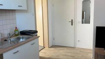 A modern kitchen with white cabinets, a wooden countertop, and a built-in sink. There is a door leading to another room and a mirror on the wall.