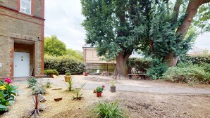 Un cortile con un grande albero, piante in vaso e un edificio in mattoni.
