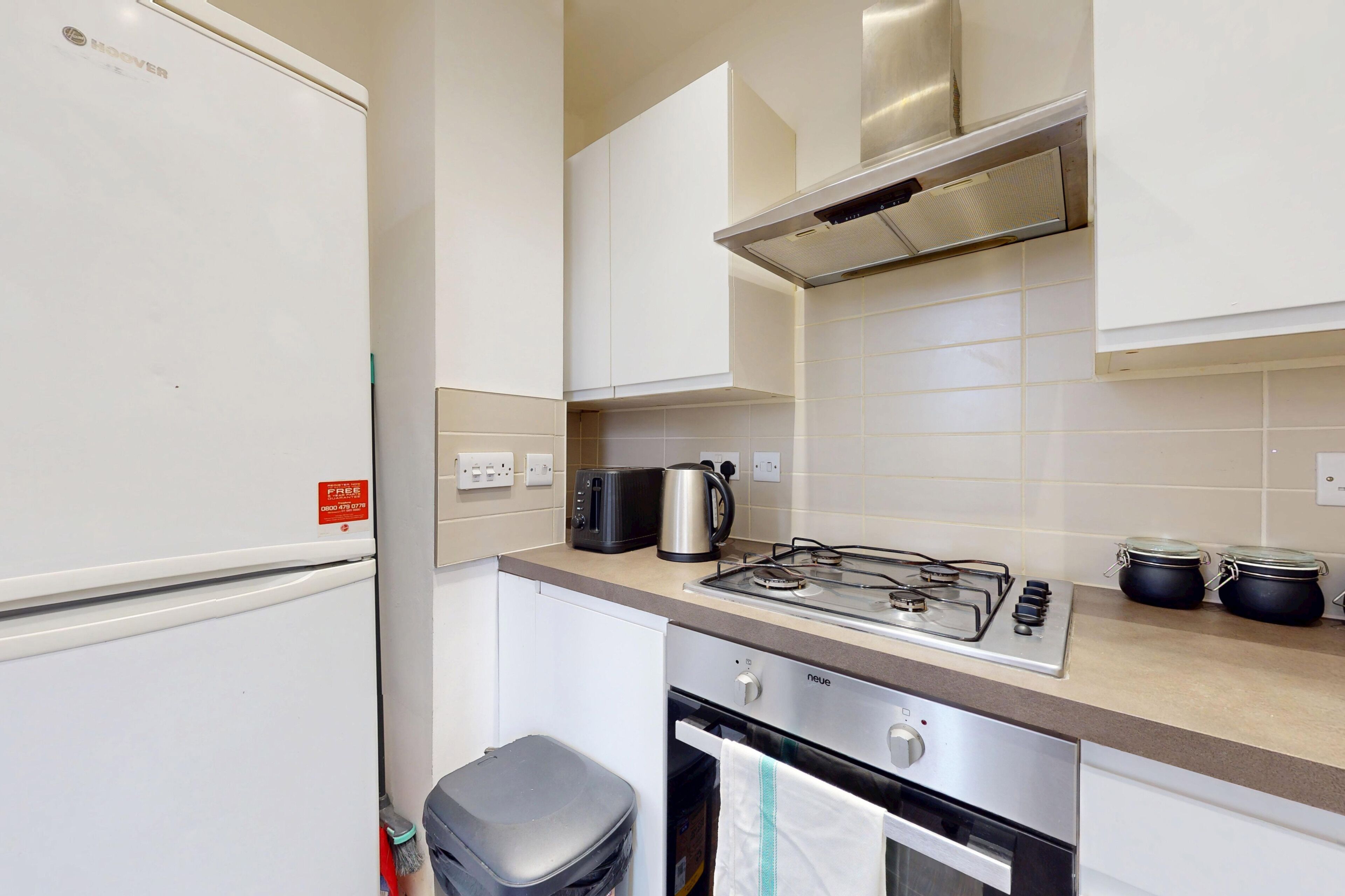 A compact kitchen with a refrigerator, a stove, a toaster, and a trash bin.