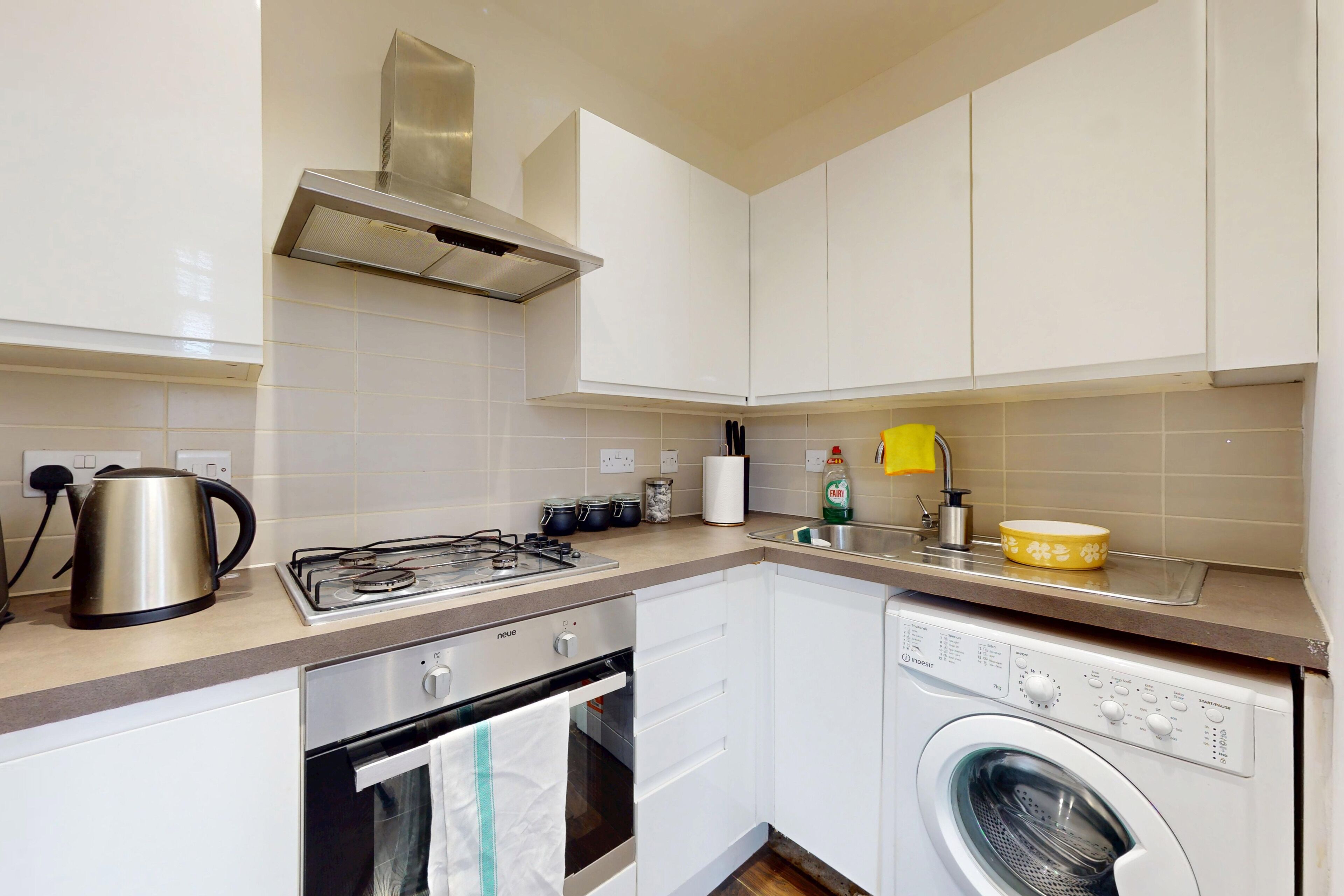 A compact kitchen with a gas stove, kettle, and a built-in washing machine.