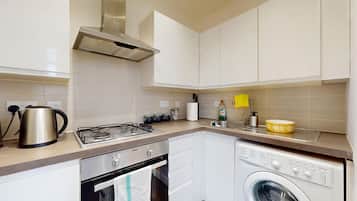 A compact kitchen with a gas stove, kettle, and a built-in washing machine.
