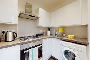 A compact kitchen with a gas stove, kettle, and a built-in washing machine. - Amazing 1BR Flat w/ Communal Garden and Parking (London)
