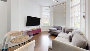 Un soggiorno moderno con televisione a schermo piatto, un tavolino da caffè in vetro, un divano e un tavolo da pranzo con sottopiatti decorati.