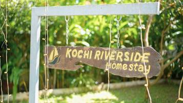 A wooden sign with the text 'KOCHI RIVERSIDE Home stay' hanging from a white structure.