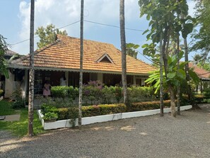 Una casa con techo de tejas, rodeada por un jardín con diversas plantas y un camino de entrada de grava.