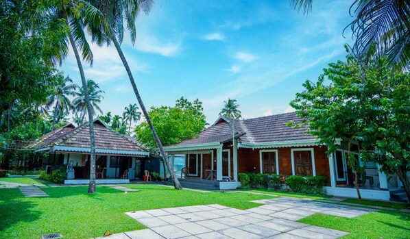 A bungalow with a tiled roof, surrounded by lush greenery and palm trees.