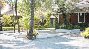 Un patio con camino de grava, árboles y un edificio con techo de tejas.