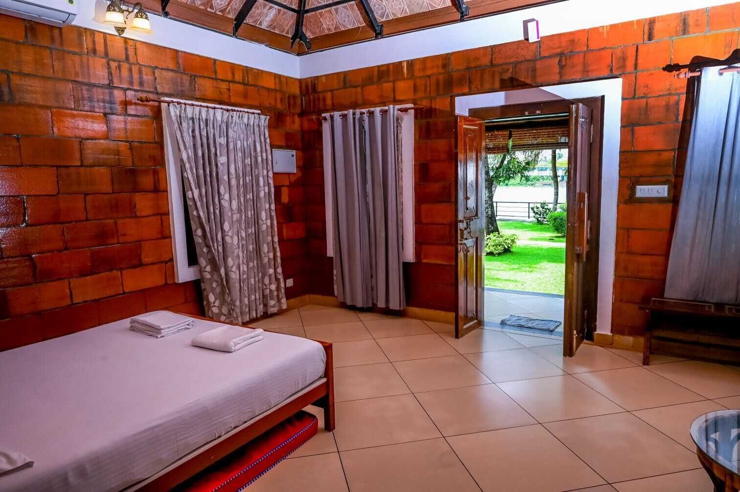 Quarto com cama, cortinas e vista para um jardim através de uma porta aberta.