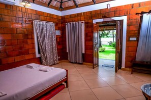 Una habitación con cama, cortinas y vista a un jardín por una puerta abierta.