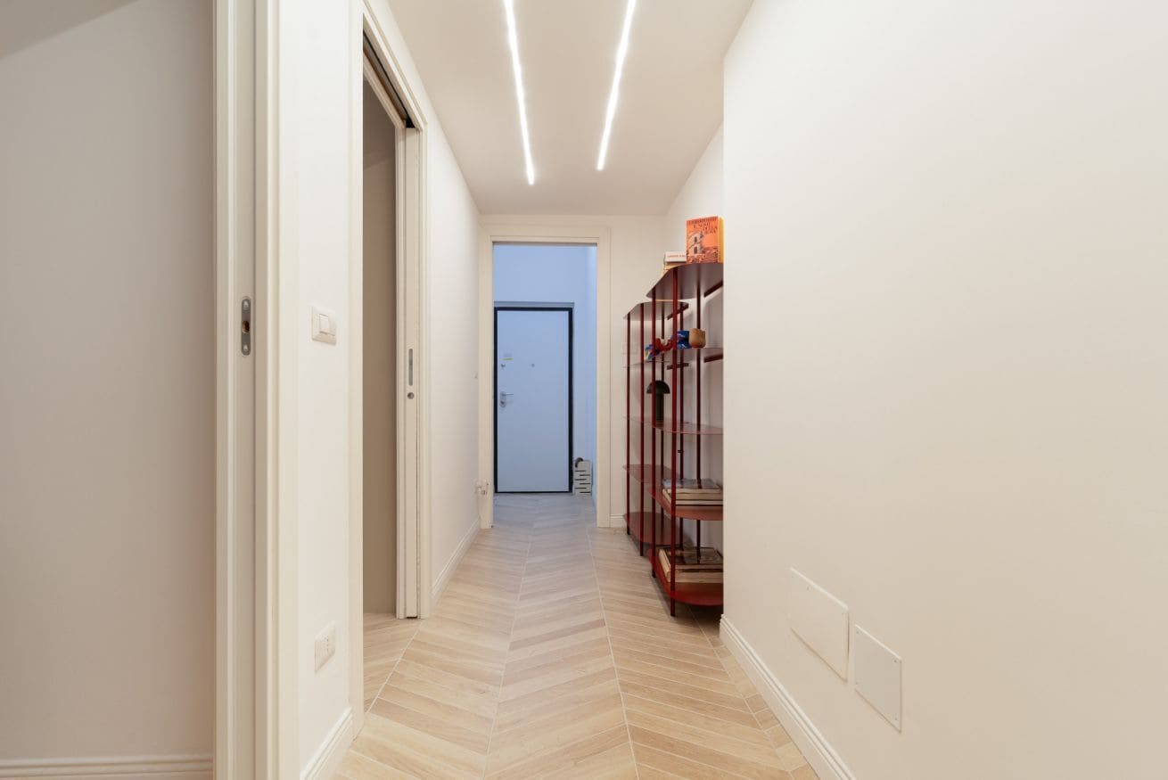 A hallway with a wooden floor, white walls, and a door at the end.