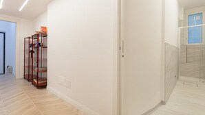 Un pasillo con suelo de madera, pared blanca y cabina de ducha de vidrio.