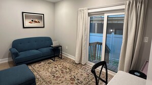 A living room with a blue sofa, a small table, a patterned rug, and a balcony with curtains. - Modern South Philly Townhome. Rooftop. Skyline Views. Home Office.  Gym (Philadelphia)