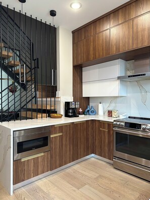 A modern kitchen with wooden cabinets, a built-in oven, a stove, and a coffee maker. - Modern South Philly Townhome. Rooftop. Skyline Views. Home Office.  Gym (Philadelphia)
