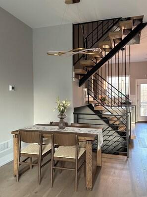 A dining area with a wooden table and chairs, a vase with flowers, and a staircase with wooden steps and metal railings. - Modern South Philly Townhome. Rooftop. Skyline Views. Home Office.  Gym (Philadelphia)