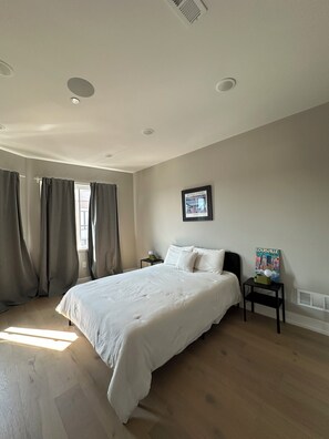 A bedroom with a large bed, a nightstand, a poster on the wall, and a window with curtains. - Modern South Philly Townhome. Rooftop. Skyline Views. Home Office.  Gym (Philadelphia)