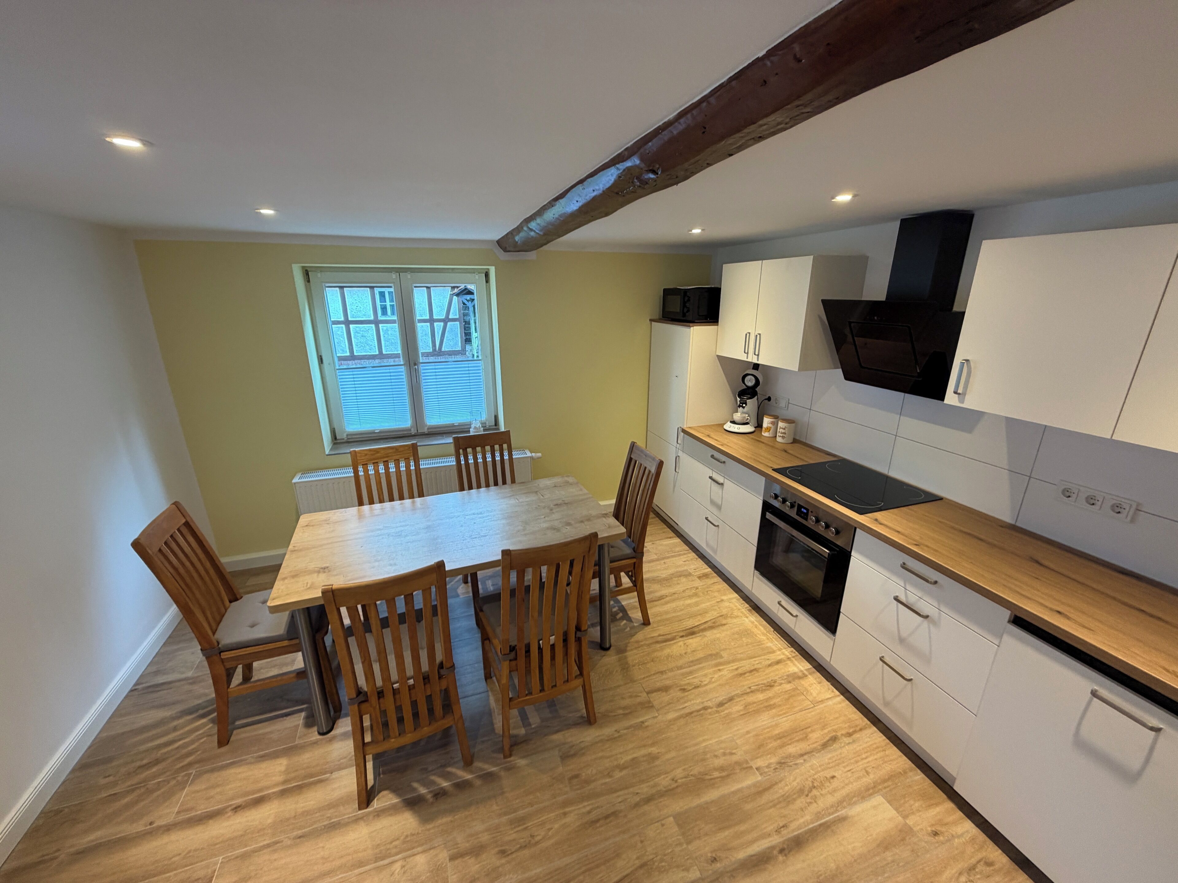 A compact kitchen with a dining area, featuring a wooden table and chairs, a built-in oven, and white cabinetry.