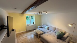 Ein Wohnzimmer mit einer Couch, einem Couchtisch, einem Fernseher und einem Fenster mit Jalousien.