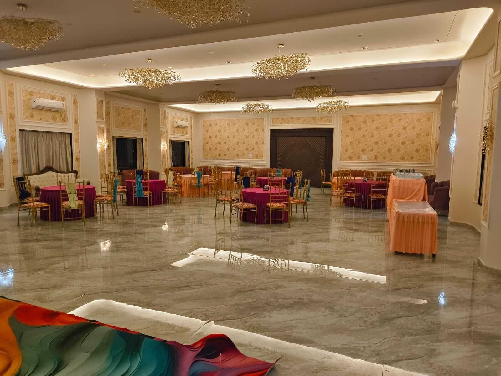 Uma ampla sala de banquetes com mesas redondas e cadeiras, um palco grande e lustres elaborados.