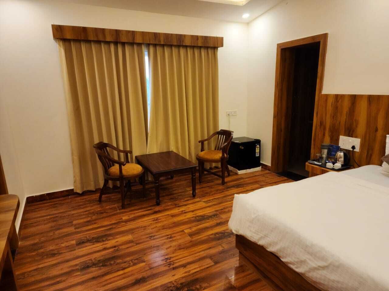A hotel room with a wooden floor, a bed, a desk, two chairs, a small table, a nightstand, and a wardrobe.