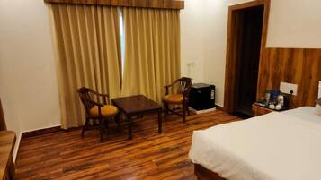 A hotel room with a wooden floor, a bed, a desk, two chairs, a small table, a nightstand, and a wardrobe.