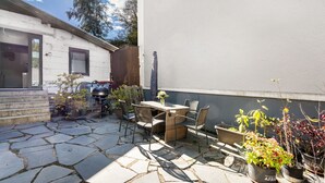 Une terrasse avec un sol en pierre, une table, des chaises et des plantes en pot.