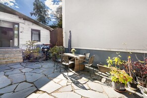 A patio with stone flooring, a table, chairs, and potted plants.