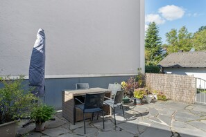 Un patio exterior con mesa y sillas, plantas en macetas y una valla de bambú.