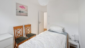 Une chambre à coucher avec un lit, deux chaises en bois, une table de chevet, une lampe et un tableau accroché au mur.