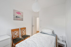 A bedroom with a bed, two wooden chairs, a bedside table, a lamp, and a painting on the wall.