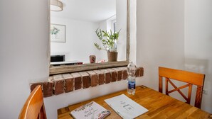 Un coin repas avec une étagère en briques, une table en bois, une chaise, une bouteille d’eau et un tableau encadré accroché au mur.