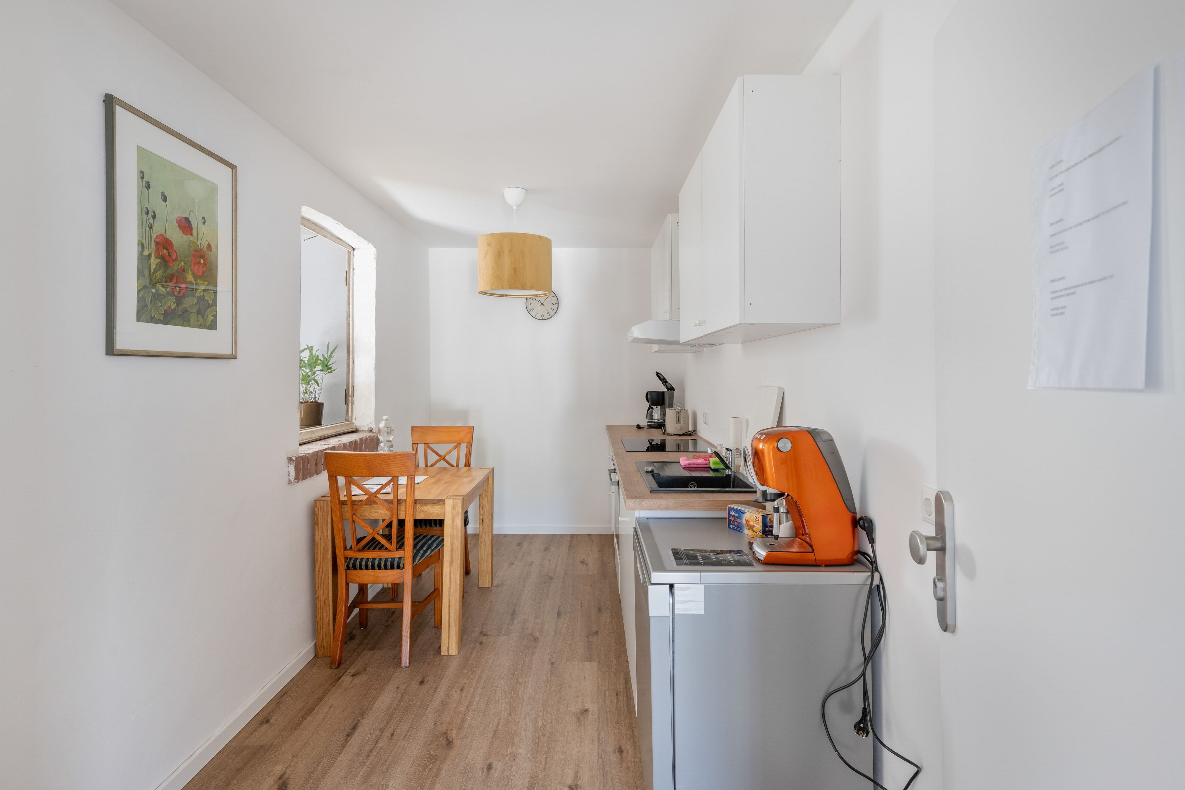 Une cuisine compacte comprenant une table à manger, des chaises, un réfrigérateur et un luminaire suspendu.