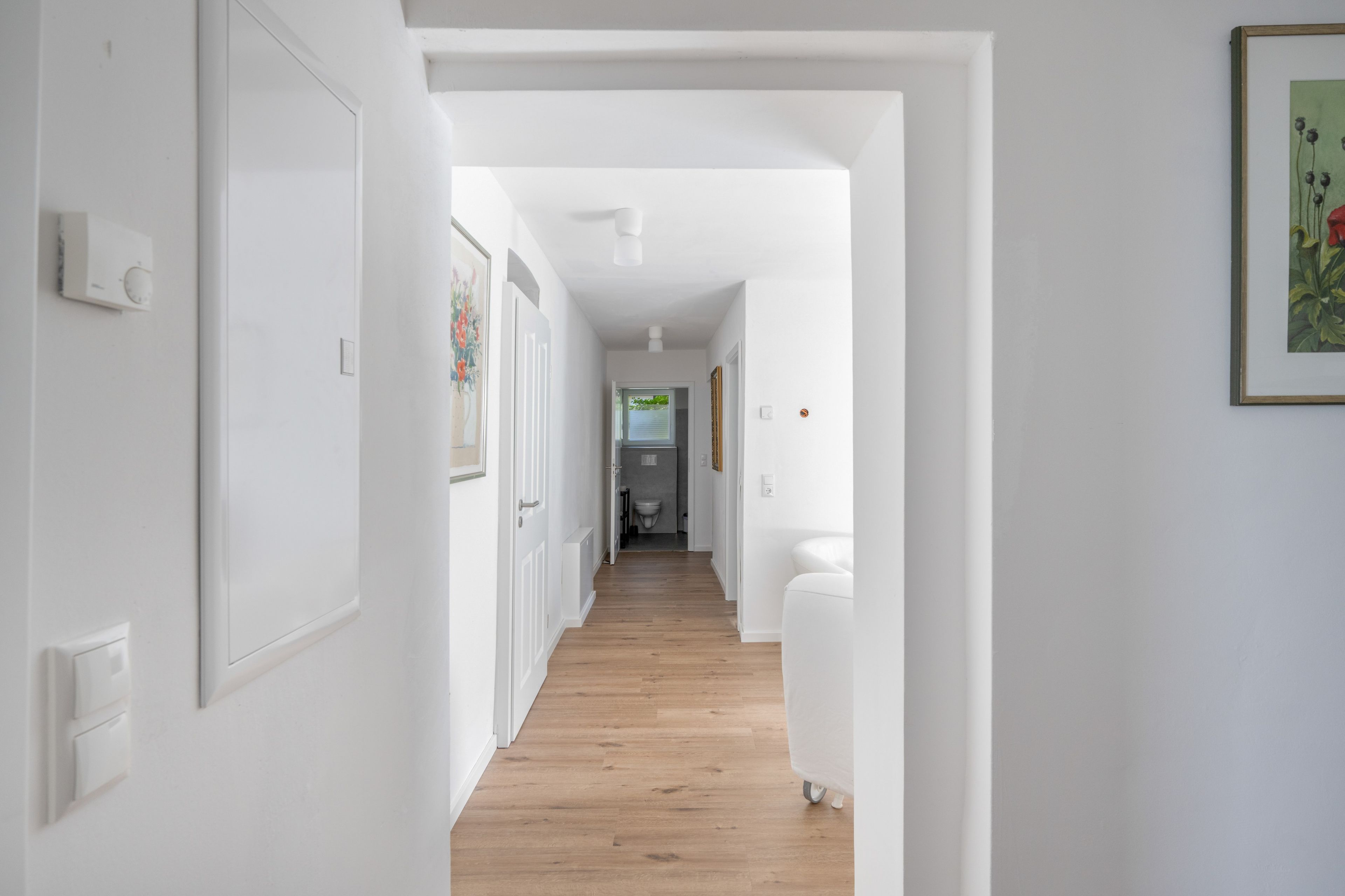 Un couloir aux murs blancs, doté d’un plancher en bois et terminé par une porte blanche.