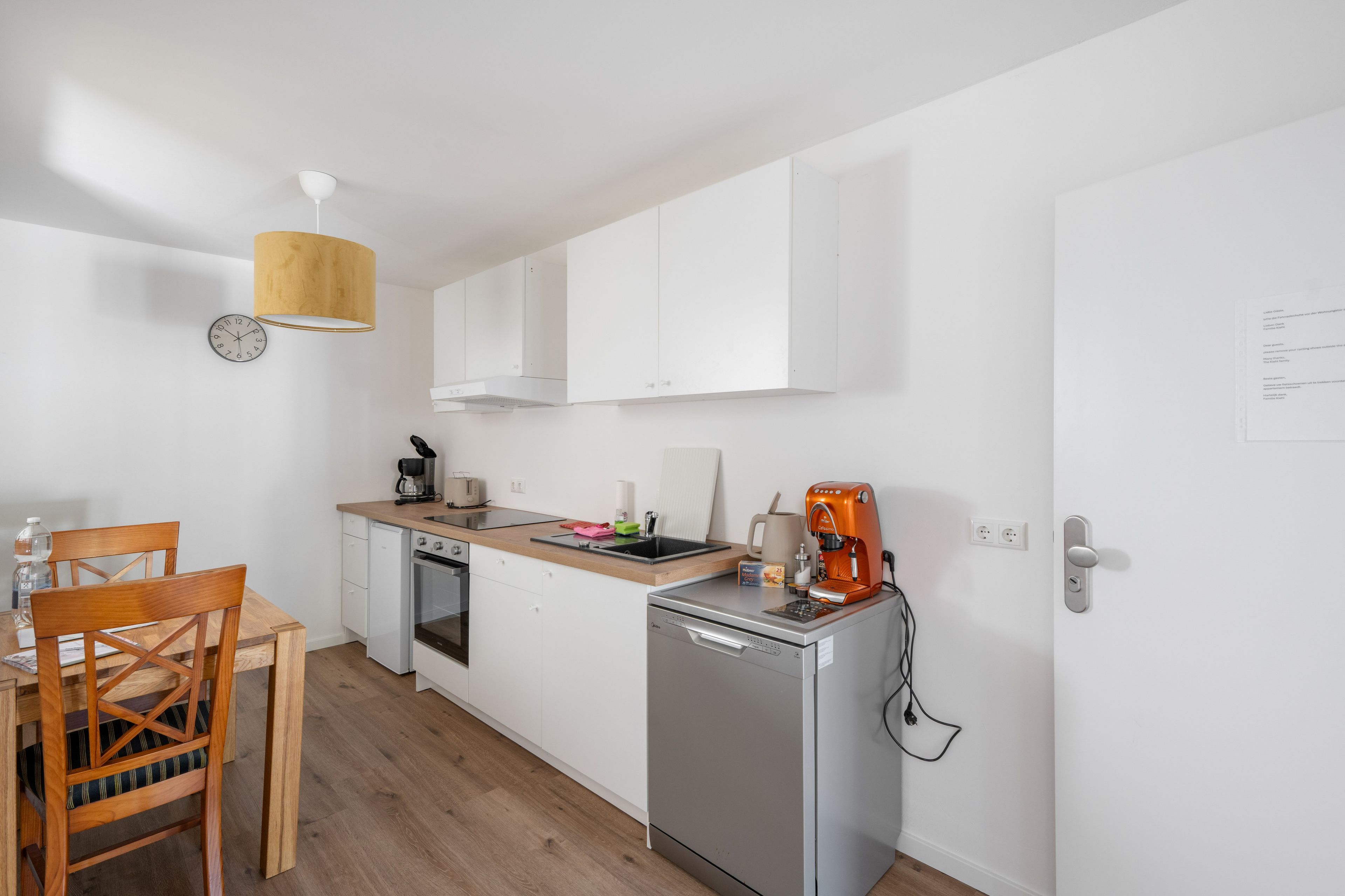 A compact kitchen with white cabinets, a coffee machine, a kettle, and a small refrigerator.